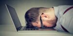 A tired businessman resting his head on a laptop keyboard, symbolizing burnout and frustration, representing the concept of 