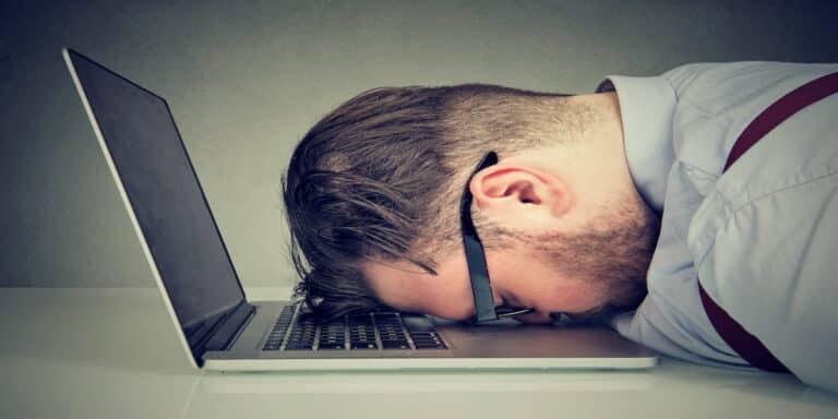 A tired businessman resting his head on a laptop keyboard, symbolizing burnout and frustration, representing the concept of 