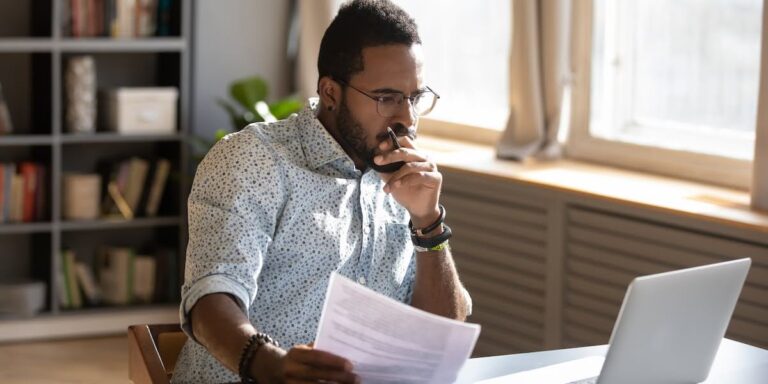 Entrepreneur reviewing documents at laptop while considering investment in coaching, reflecting on the question are business coaches worth it.