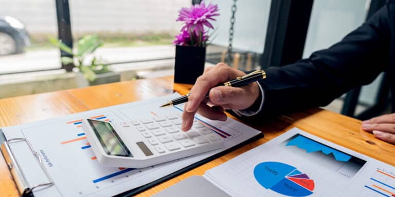 A man using a calculator and reviewing charts and paperwork as part of his business budget planner, carefully organizing financial details.