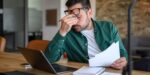 Stressed entrepreneur reviewing documents at laptop, illustrating common business mistakes that small business owners make.