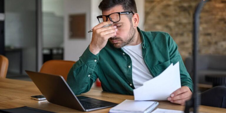 Stressed entrepreneur reviewing documents at laptop, illustrating common business mistakes that small business owners make.