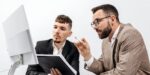 Two professionals reviewing plans on computer during meeting to find a business coach who aligns with company goals