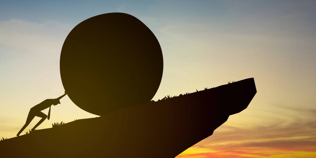 Silhouette of a person pushing a large boulder uphill symbolizing a growth plateau in business