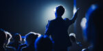 Business speaker demonstrating organizational leadership principles while presenting to engaged audience in dramatic blue lighting