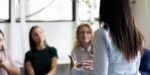 Businesswoman leading a small group discussion, viewed from behind, illustrating key concepts in the psychology of leadership