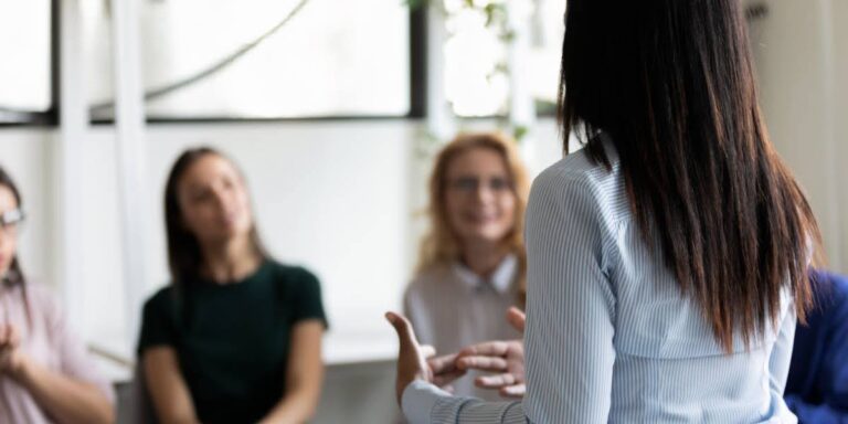 Businesswoman leading a small group discussion, viewed from behind, illustrating key concepts in the psychology of leadership