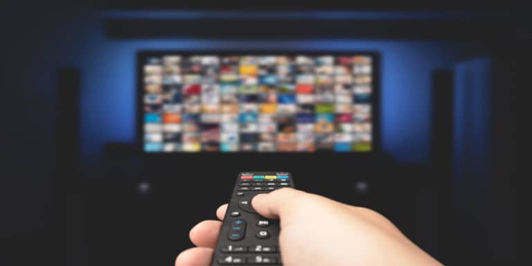 A hand holding a remote control in front of a TV screen filled with streaming options, symbolizing the subscription model in recurring revenue businesses. This visual represents the concept of consistent, predictable income through subscription-based services.