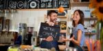 Smiling café owners holding a sign that says “We’re open,” representing optimism while asking why do most small businesses fail and how to succeed.