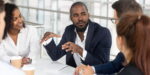 Business leader explaining why is leadership important during team meeting with diverse professionals in modern office setting